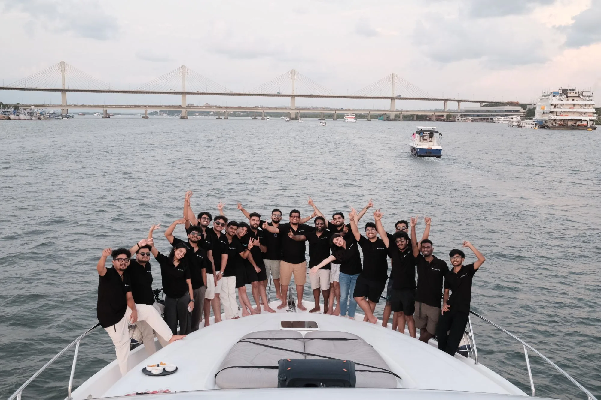 The whole Outbox team on the bow of the boat, arms up and waving, the bridge behind them
